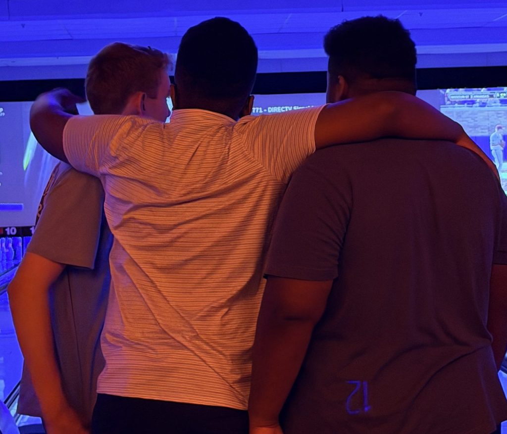 The three founders of Next Generation Scholars, seen from behind with their arms around each other's shoulders